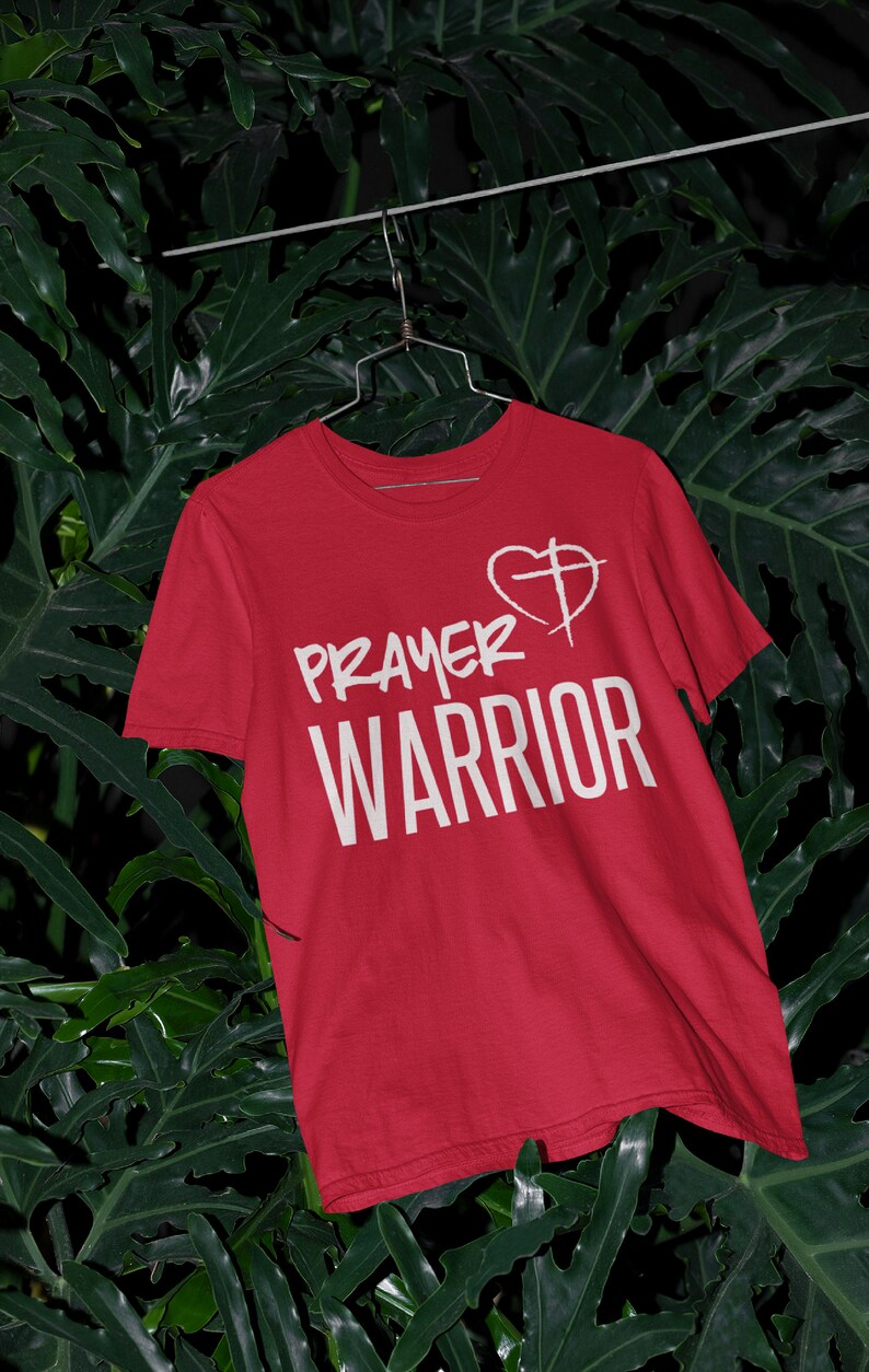 K&ouml;nnte beinhalten: Rotes T-Shirt mit wei&szlig;em Text "PRAYER WARRIOR" und einem wei&szlig;en Herz mit einem Kreuz darin.
