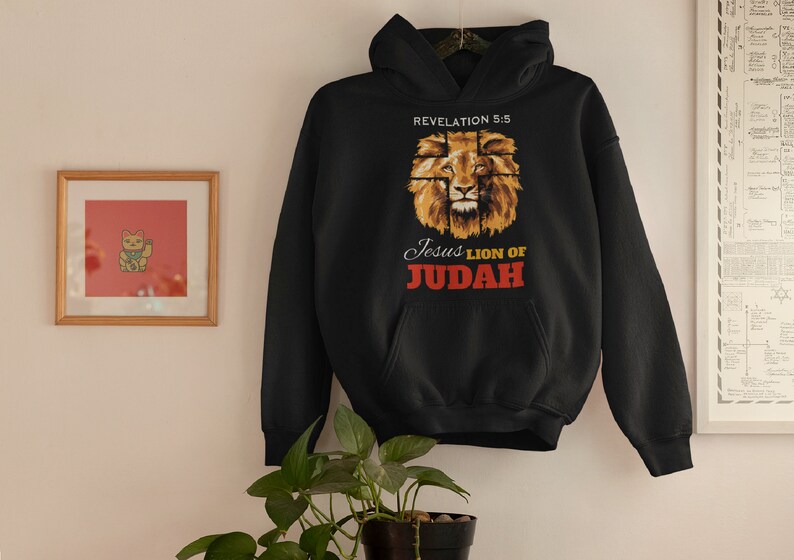 Może przedstawiać: Czarna bluza z kapturem z grafiką przedstawiającą twarz lwa z nadrukiem "Revelation 5:5 Jesus Lion of Judah" na przodzie.