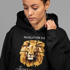 Może przedstawiać: Czarna bluza z kapturem z grafiką głowy lwa, na kt&oacute;rej nałożony jest krzyż. Tekst "Revelation 5:5" znajduje się nad lwem, a tekst "Jesus Lion of Judah" pod lwem.