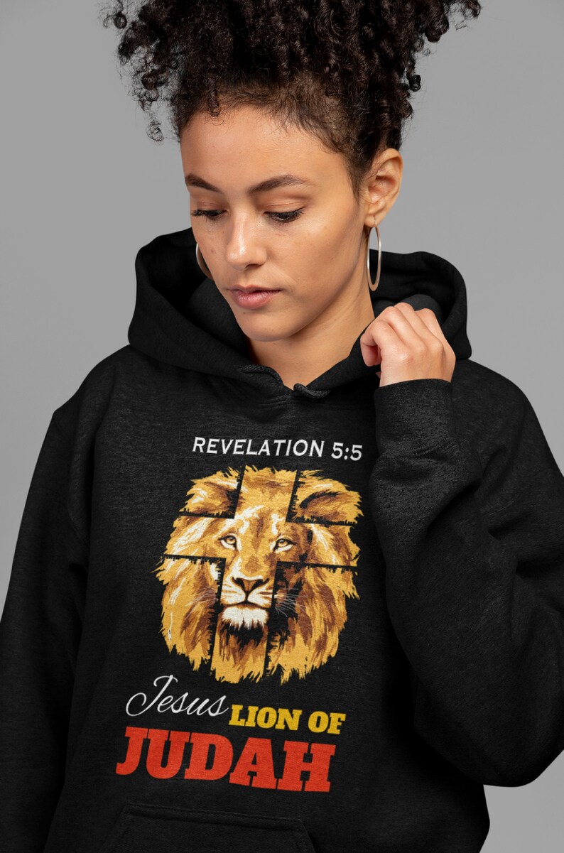 Może przedstawiać: Czarna bluza z kapturem z grafiką głowy lwa, na kt&oacute;rej nałożony jest krzyż. Tekst "Revelation 5:5" znajduje się nad lwem, a tekst "Jesus Lion of Judah" pod lwem.