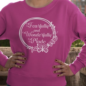 May include: A pink sweatshirt with a white graphic design that says "Fearfully and Wonderfully Made" in a circle with floral accents and butterflies.
