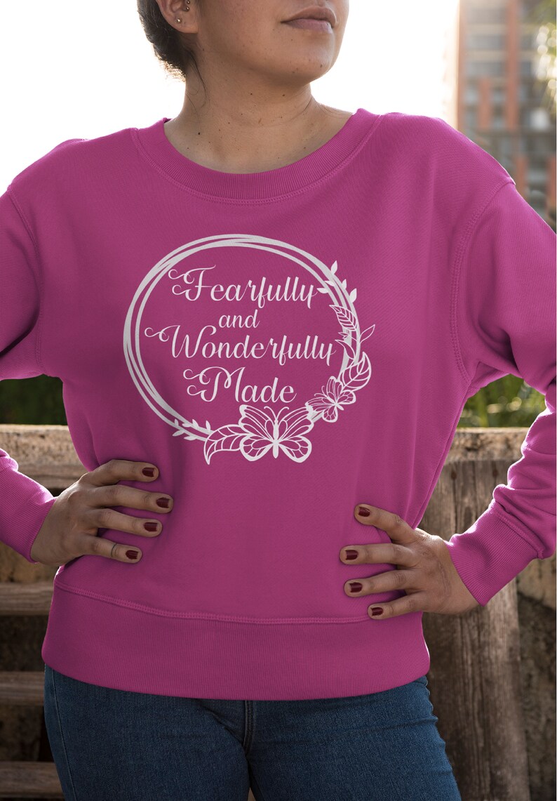 May include: A pink sweatshirt with a white graphic design that says "Fearfully and Wonderfully Made" in a circle with floral accents and butterflies.