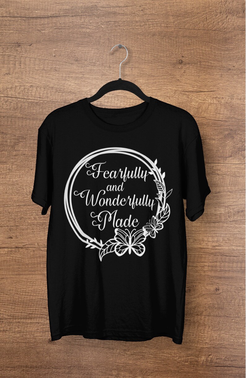 May include: Black t-shirt with a white graphic design of a circle with a floral border and butterflies. The text inside the circle reads "Fearfully and Wonderfully Made".
