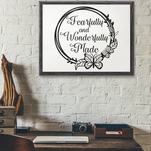May include: A black and white framed print with a floral wreath and butterfly design. The text inside the wreath reads "Fearfully and Wonderfully Made".
