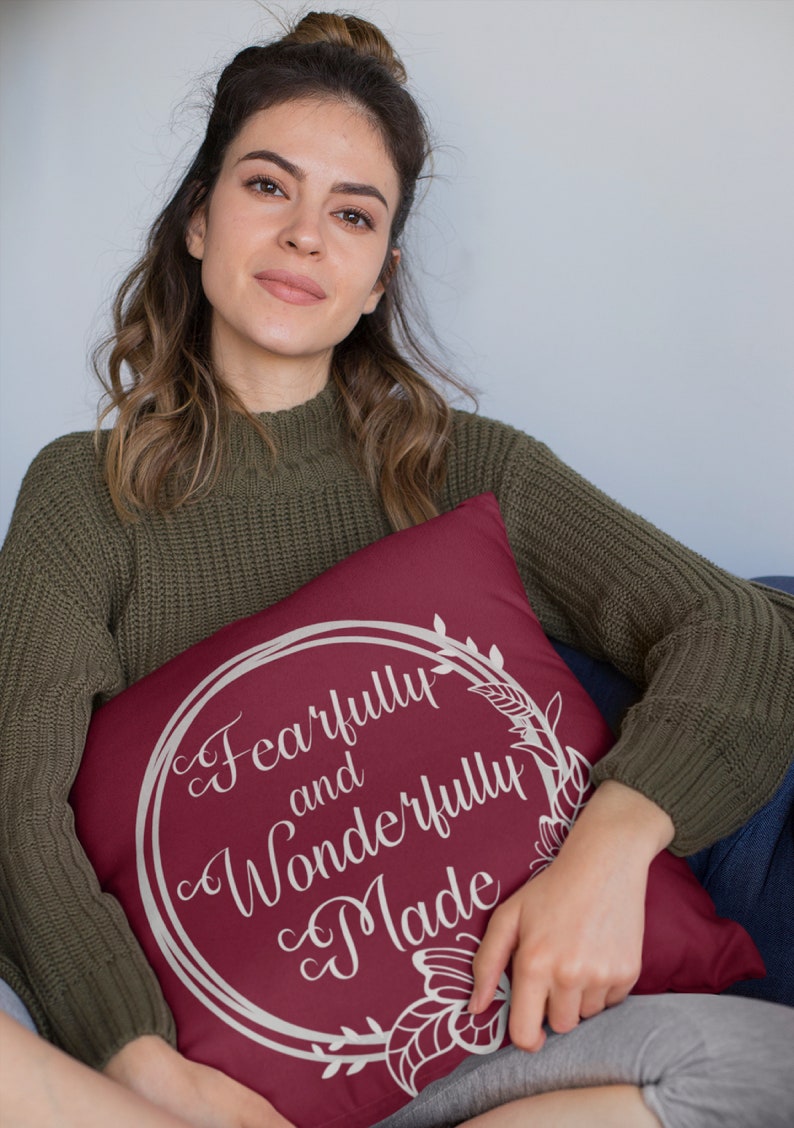 May include: A maroon throw pillow with a white floral wreath design and the text "Fearfully and Wonderfully Made".