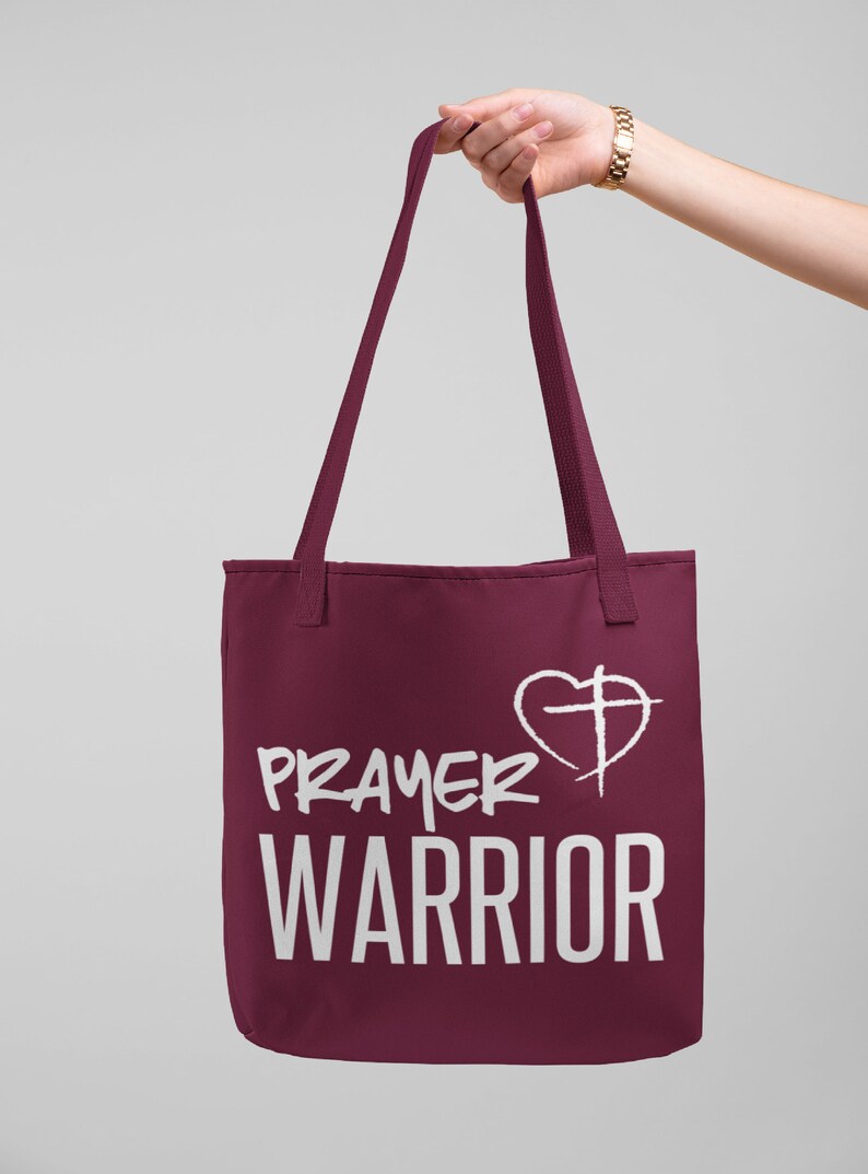 K&ouml;nnte beinhalten: Eine weinrote Tragetasche mit wei&szlig;em Text, der "PRAYER WARRIOR" lautet, und einem wei&szlig;en Herzen mit einem Kreuz darin.
