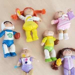 Puede incluir: Un conjunto de seis figuras de Cabbage Patch Kids. Las figuras son todas de diferentes colores y tienen diferentes atuendos. Todas llevan diferentes accesorios, como un balón de fútbol, una cuchara y un osito de peluche.