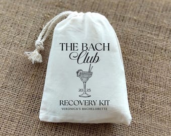 May include: White cotton drawstring bag with the text "The Bach Club" in black cursive lettering. A black and white illustration of a margarita glass with a lime wedge is below the text. The text "Recovery Kit" is below the illustration, and the text "Veronica's Bachelorette" is below that.