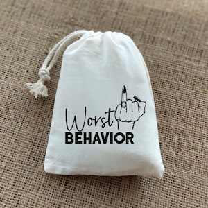 May include: White cotton drawstring bag with black text that reads "Worst Behavior" and a black illustration of a hand giving the middle finger with a ring on it.