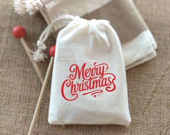 May include: A white drawstring bag with the words "Merry Christmas" printed in red cursive lettering. The bag is sitting on a burlap surface.