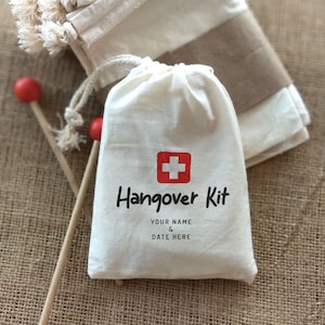 May include: A white cotton drawstring bag with a red cross and the text "Hangover Kit" printed on it. The bag is on a brown burlap surface. The text below the kit name says "Your Name & Date Here".