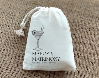 Puede incluir: Bolsa de algodón blanco con cordón de ajuste, con una ilustración en blanco y negro de una copa de margarita y el texto "MARGS & MATRIMONY VERONICA'S BACHELORETTE"