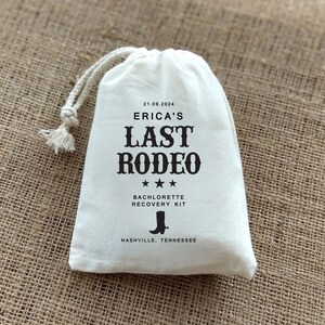 May include: White drawstring bag with black text that reads "Erica's Last Rodeo" with three stars below the text. The text "Bachelorette Recovery Kit" is below the stars. A black boot icon is below the text and the text "Nashville, Tennessee" is below the boot icon. The date "21.09.2024" is at the top of the bag.