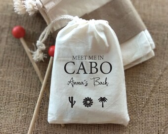 May include: White cotton drawstring bag with the text "Meet me in Cabo Anna's Bach" and three black icons: a cactus, a sun, and a palm tree.