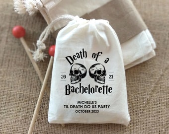 May include: White cotton drawstring bag with the text "Death of a Bachelorette" printed in black. The bag also features two black skull illustrations and the text "Michelle's Til Death Do Us Party October 2023".