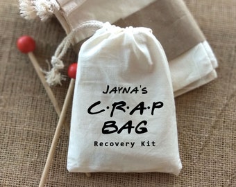 以下が含まれることがあります： 黒い文字で「Jayna's C.R.A.P BAG Recovery Kit」と書かれた白い綿の巾着袋です。