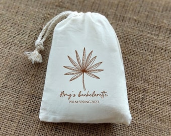 May include: A white cotton drawstring bag with a brown palm tree design and the text "Amy's bachelorette Palm Spring 2023".