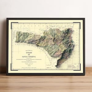 May include: Framed vintage map of Santa Catarina, Brazil, in a black frame. The map features detailed topography with shades of green, brown, and beige. Text on the map includes "Estado de Santa Catarina" and other Portuguese text.