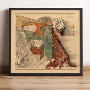 Może przedstawiać: Oprawiona mapa geologiczna Egiptu, z trójwymiarowym reliefem. Mapa przedstawia różne kolory, w tym beżowy, pomarańczowy, zielony i czerwony, reprezentujące różne formacje geologiczne. Mapa jest w czarnej ramie i spoczywa na drewnianej powierzchni.
