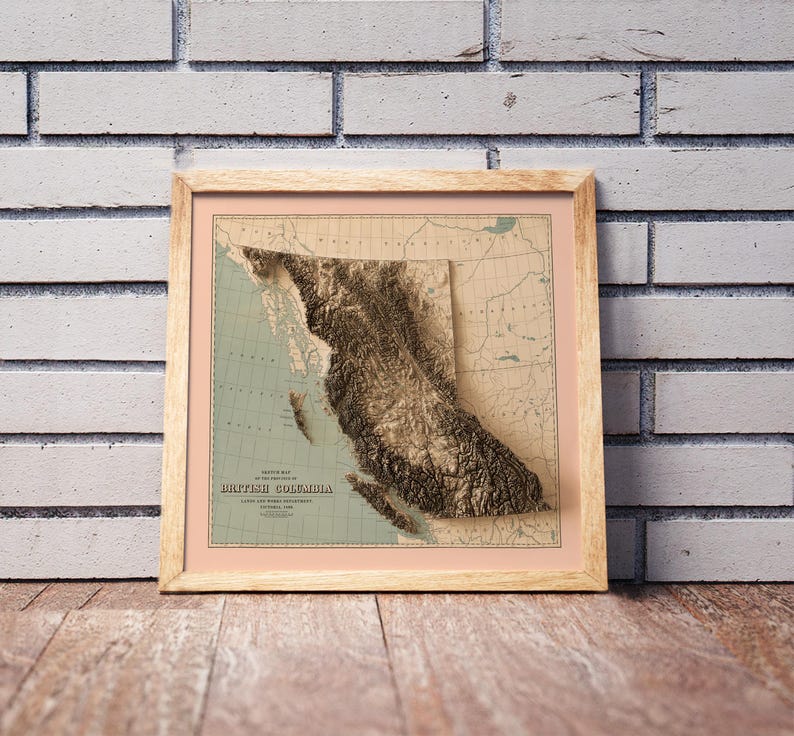Vintage British Columbia Canada shaded relief map in a wooden frame. Realistic terrain art print for home decor, displayed against a brick wall