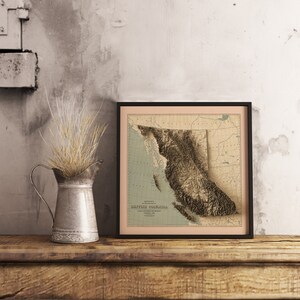 Vintage British Columbia shaded relief map in black frame. Realistic terrain art print for home decor, displayed on rustic wooden table