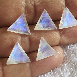Può includere: Cinque cabochon triangolari di pietra di luna arcobaleno iridescente, ognuno con un diverso motivo di blu e bianco.