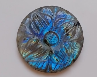 May include: A round, carved labradorite gemstone with a blue, green, and gold iridescent sheen. The gemstone has a flower-like design carved into its surface.