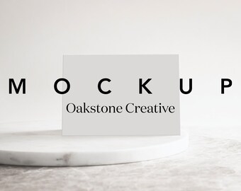 Puede incluir: Una tarjeta blanca con la palabra "MOCKUP" en letras negras y el texto "Oakstone Creative" en letras negras sobre una superficie de mármol blanco.