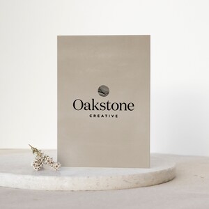 May include: A beige card with a black circle logo and the text "Oakstone Creative". The card is sitting on a white marble surface.