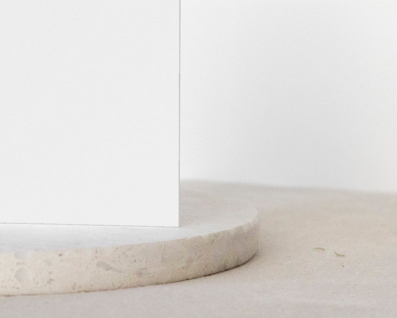 May include: A white, round, textured pedestal with a white square on top. The pedestal is made of a light-colored material, possibly concrete or stone.
