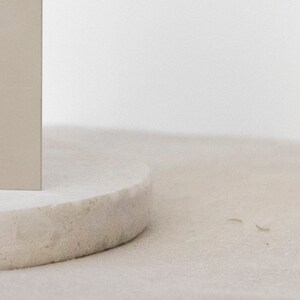 May include: A close-up of a round, light gray, textured pedestal with a light beige rectangular object on top.
