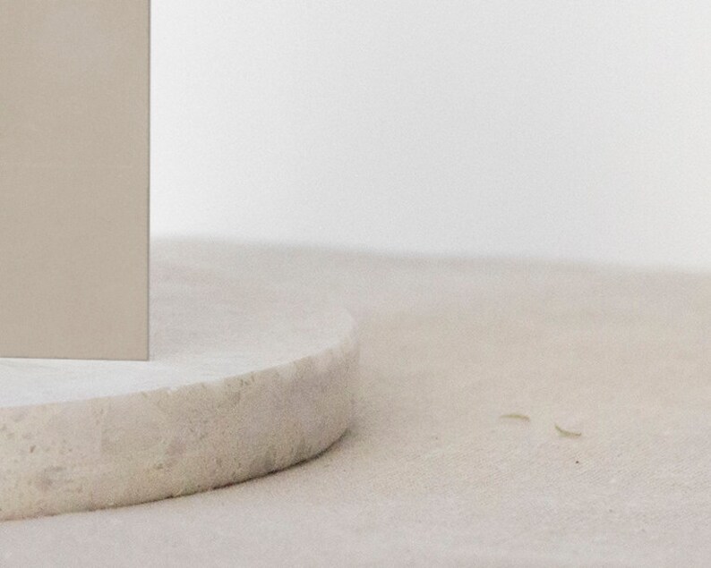 May include: A close-up of a round, light gray, textured pedestal with a light beige rectangular object on top.