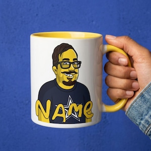 Op de afbeelding: Een witte keramische mok met een gele binnenkant en handvat, voorzien van een cartoonachtige illustratie van een geelkleurig persoon met donker haar, een bril en een snor, gekleed in een donkerblauw t-shirt met een witte ster en het woord NAME.