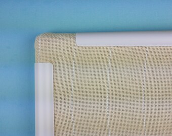 May include: Close-up of the top edge of a beige canvas with white stitching. The canvas is framed with a white plastic border.