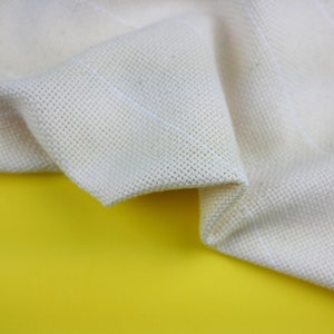 May include: A close-up of a white fabric with a textured weave. The fabric is folded and draped over a yellow surface.