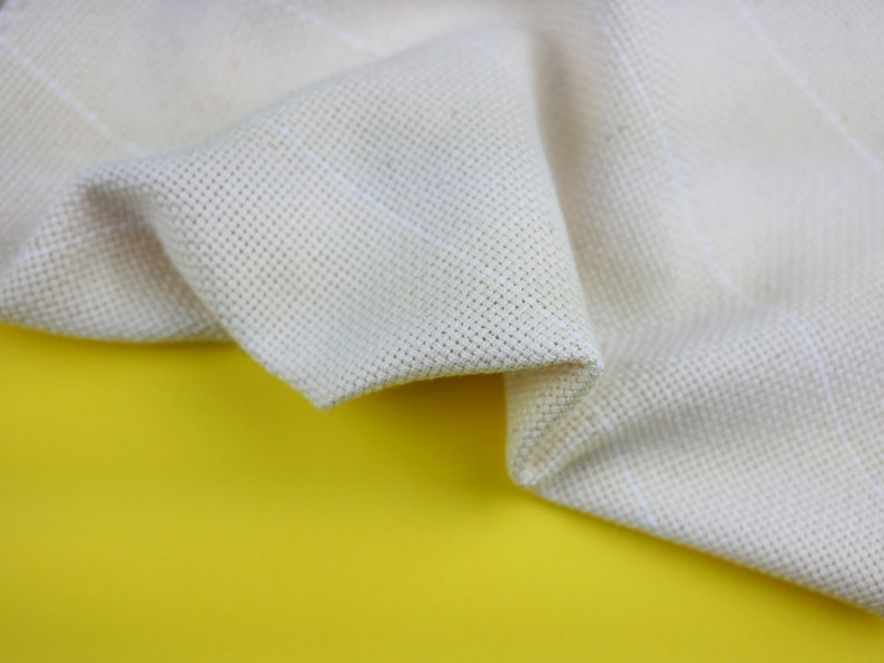 May include: A close-up of a white fabric with a textured weave. The fabric is folded and draped over a yellow surface.
