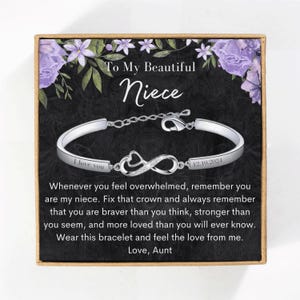 May include: A silver bracelet with an infinity symbol charm and the words "I love you" and "12.10.2024" engraved on it. The bracelet is in a gift box with a message to a niece that says "To My Beautiful Niece" and "Whenever you feel overwhelmed, remember you are my niece. Fix that crown and always remember that you are braver than you think, stronger than you seem, and more loved than you will ever know. Wear this bracelet and feel the love from me. Love, Aunt"