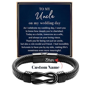 May include: A black braided leather bracelet with a stainless steel clasp and an infinity knot design. The bracelet is personalized with the name "Ethan" and the words "Custom Name". A navy blue card with text that reads "To My Uncle on my wedding day" is in the background.