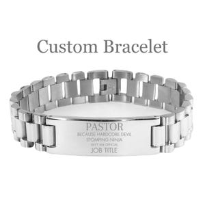May include: A silver-colored bracelet with a rectangular plate engraved with the word "PASTOR" and the text "BECAUSE HARDCORE DEVIL STOMPING NINJA ISN'T AN OFFICIAL JOB TITLE". The bracelet is labeled "Custom Bracelet".