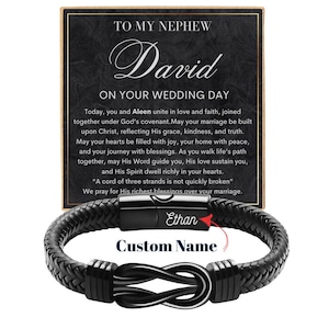 May include: A black leather bracelet with a braided design and a silver-colored infinity knot clasp. The bracelet has a magnetic clasp with the name "Ethan" engraved. A card with text that reads "TO MY NEPHEW David ON YOUR WEDDING DAY" is behind the bracelet.