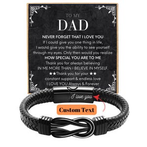May include: Black braided leather bracelet with a magnetic clasp and a decorative infinity knot. A card behind the bracelet reads "TO MY DAD" with a heartfelt message. The card also has decorative flourishes.