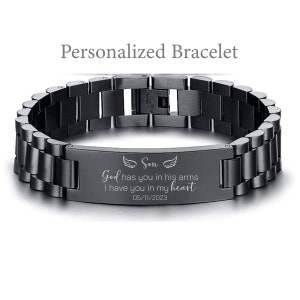 May include: Black stainless steel bracelet with an engraved plate that reads "Son, God has you in his arms, I have you in my heart, 05/11/2023". The plate also features two small angel wings.