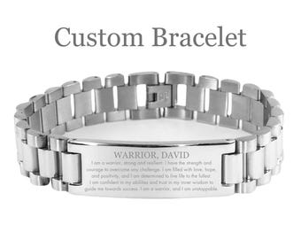 May include: A silver-toned custom bracelet with the text "Custom Bracelet" at the top. The bracelet features a rectangular plate engraved with the words "WARRIOR, DAVID" and an inspirational message. The bracelet is made of linked metal segments.