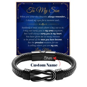 May include: A black braided leather bracelet with a black metal infinity knot centerpiece and a magnetic clasp engraved with the name Ethan. The bracelet is displayed in front of a blue card featuring the text To My Son and a sentimental message.
