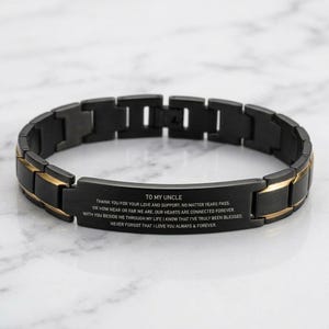 May include: A black and gold-toned link bracelet featuring a central rectangular plate engraved with the text: TO MY UNCLE. THANK YOU FOR YOUR LOVE AND SUPPORT. NO MATTER YEARS PASS. OR HOW NEAR OR FAR WE ARE. OUR HEARTS ARE CONNECTED FOREVER.
