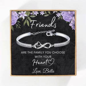 May include: A silver bracelet with an infinity symbol charm and the words "Friends are the family you choose with your heart" engraved on it. The bracelet is in a black box with a floral design and the words "Love, Bella" on the bottom.