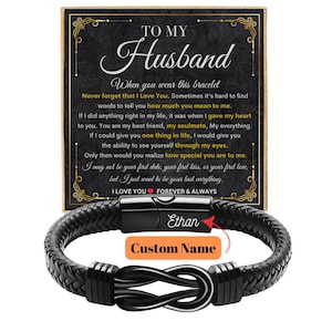 May include: Black braided leather bracelet with a silver-tone clasp and an infinity symbol design. The bracelet has a personalized name plate and comes with a card that reads "To My Husband". The card includes a heartfelt message.