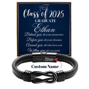 May include: Black leather bracelet with an infinity knot design and a silver metal clasp. The bracelet comes in a box with a blue background and the text "Class of 2025 GRADUATE Ethan" and a graduation cap icon. The box also includes the text "Behind you all your memories, Before you all your dreams, Around you all who love you, Within you all you need".