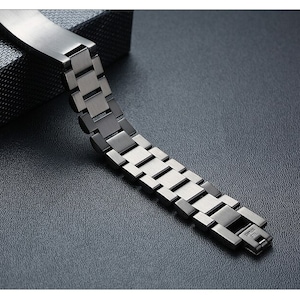 May include: A silver metal watch band with a link style design. The band is made of multiple connected links.