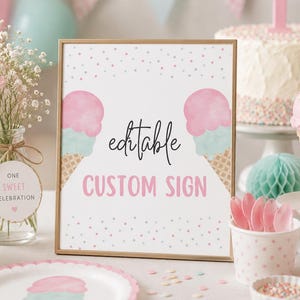 May include: A decorative sign with the text "editable CUSTOM SIGN" in pink and black, featuring ice cream cone designs. The sign is part of a party setting, including a cake, balloons, and flowers, indicating a first birthday celebration.